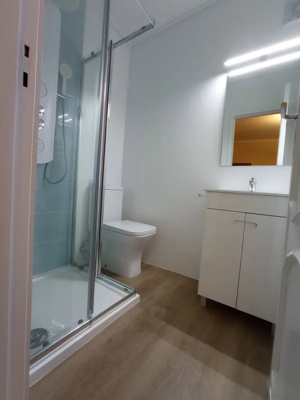 Casa de banho remodelada com base de duche, móvel branco e pavimento em madeira